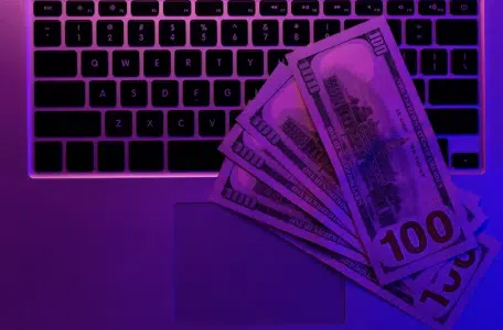 Laptop and paper money in neon lighting top view